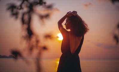 Young beautiful sensual woman in a stylish dress with an open back is standing on the seashore at...