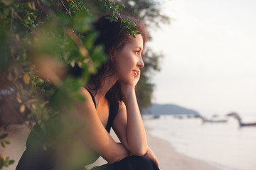 Portrait of a beautiful young woman with dark hair in a frame of branches and green leaves, on the coast, sensitive portrait of a natural beauty
