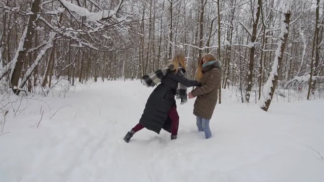 two happy adult female siblings are playing in snowy forest in winter day, one is pushing other