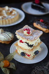 Tea and sweets on a dark background, Mille-feuille, Eclairs, Tart, Decorative with flowers, Selective focus, Closeup