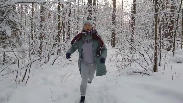 scared adult woman is fleeing in winter forest in daytime, looking back, she is tired, stopping