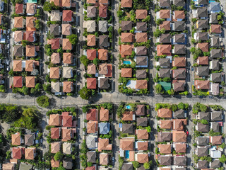 Aerial top down view flying over city showing neighborhood family houses real estate with orange red roofs and gardens