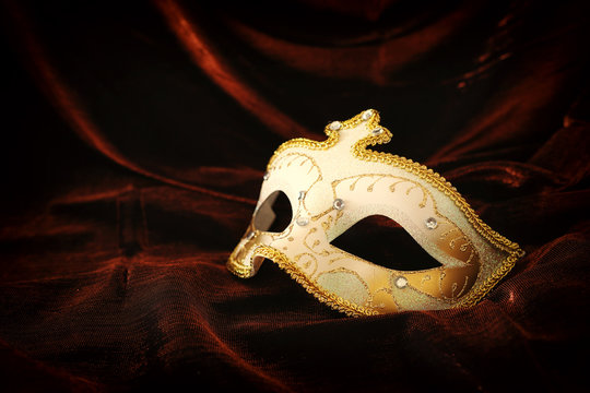 Photo of elegant and delicate gold, white venetian mask over dark velvet and silk background.