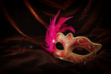 Photo of elegant and delicate gold, red venetian mask over dark velvet and silk background.