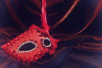 Photo of elegant and delicate red venetian mask over dark velvet and silk background.