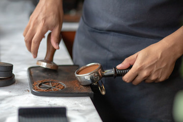 Barista using a tamper to press ground coffee into a portafilter. Close up photo
