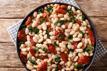 Spicy bean stew with spinach, garlic and dried tomatoes closeup on a plate. Horizontal top view