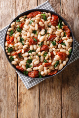 Vegetarian stew of white beans with spinach, garlic and dried tomatoes close-up on a plate. Vertical top view