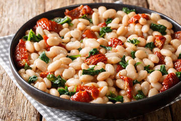Healthy meal of white beans with spinach, garlic and sun-dried tomatoes closeup on a plate....