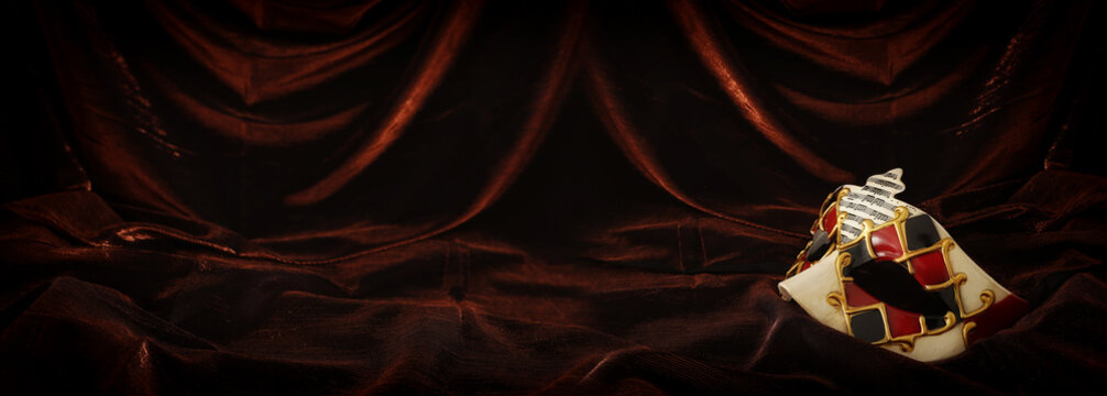 Photo of elegant and delicate venetian mask over dark velvet and silk background.