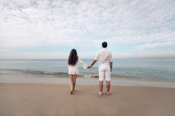  Young Couple looking at the sea and overcast sky in white clothing. Back view. Phuket. Thailand. Trip to warm destination.