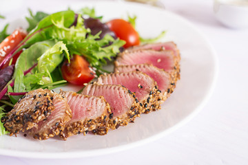 Japanese traditional salad with pieces of medium-rare grilled Ahi tuna and sesame with fresh vegetable salad on a plate. Authentic Japanese food.