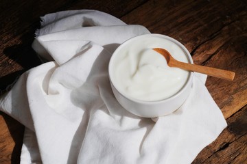 Natural homemade plain organic yogurt in white bowl and wood spoon on wood texture background