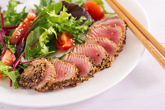 Japanese traditional salad with pieces of medium-rare grilled Ahi tuna and sesame with fresh vegetable salad on a plate. Authentic Japanese food.