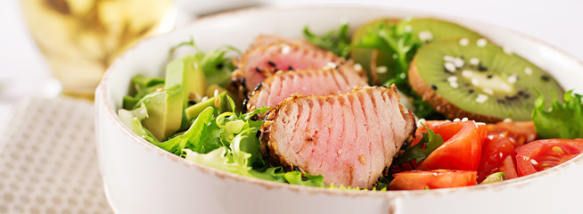 Salad. Poke bowl. Buddha bowl. Traditional salad with pieces of medium-rare grilled Ahi tuna and sesame with fresh vegetables and rice on a plate. Top view. Flat lay. Banner. Copy space.