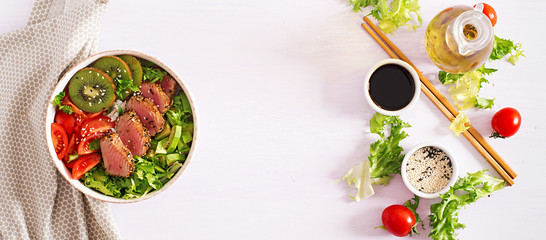 Poke bowl. Buddha bowl. Traditional salad with pieces of medium-rare grilled Ahi tuna and sesame with fresh vegetable salad and rice on a plate. Top view. Copy space. Banner