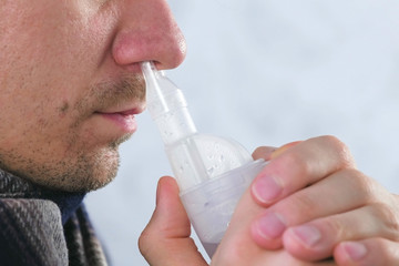 Sick man inhaling through inhaler nozzle for nose. Close-up nose, side view. Use nebulizer and inhaler for the treatment.