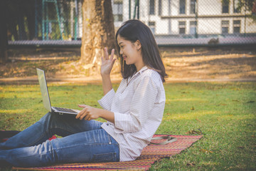 The asia woman is playing computer on a notebook.She sits and play laptop in park.