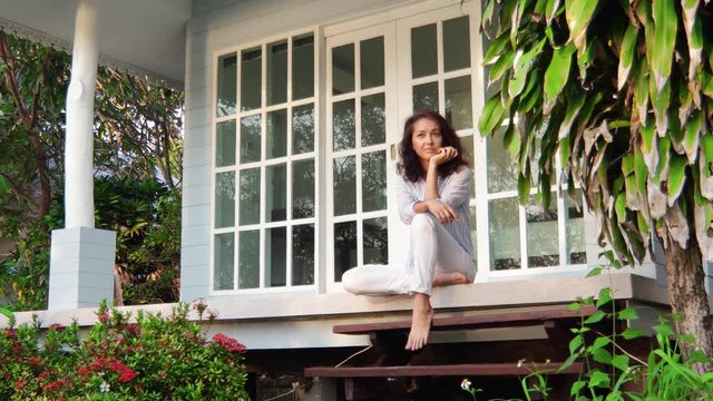 A young beautiful woman is sitting on the porch of her country house and thoughtfully enjoying the view.