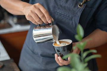 Professional barista pouring steamed milk into coffee cup making beautiful latte art Rosetta pattern