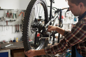 Man mechanic working in bicycle repair shop, technician repairing modern bike using special tool