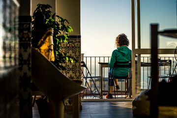 Backside view on woman in green sweatshirt sitting on the terrace and reading or drinking coffee. Enjoying the sunny early morning. Lisbon, Portugal. - 247118135