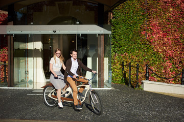 Young smiling tourist couple, handsome man and pretty long-haired blond woman cycling tandem bike on bright sunny day