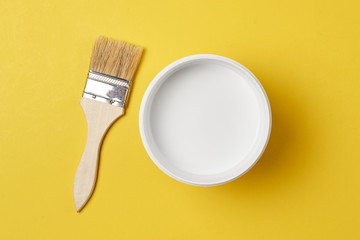Brush and paint can with white color on a yellow background, top view