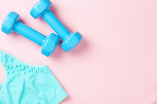 Blue dumbbells and sport bra on a pink background, top view with copy space. Fitness concept