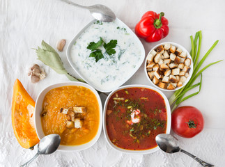 3 plates with soups, top view, borsch, yogurt soup with greens, pumpkin soup, spoons, herbs, vegetables, tomato, pumpkin, pepper, bay leaf, garlic,