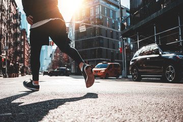 Close-up of athlete legs running through the New York streets. Sporty man fast running early morning in sunny day through urban city