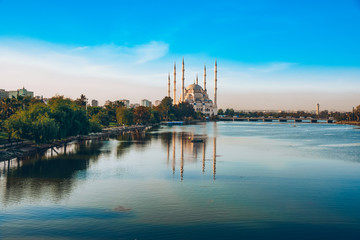 Fototapeta na wymiar City of Adana, Turkey. Sabanci Central Mosque in Adana with Seyhan River and Trees. Mosque has reflections from Seyhan river in sunny day with blue clean sky