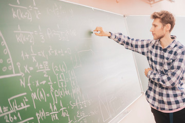 persons hand hold chalk and write mathematic calculations on a board b