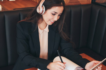 Beautiful charming brunette smiling asian girl in headphones with tablet in cafe, student,...