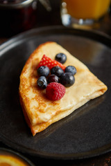 Tasety homemade pancake on black ceramic plate. Placed on dark rusty table. With fresh fruits, orange juice and marmalade. Top view, Flat lay.