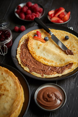 Delicious homemade pancakes on black ceramic plate. Placed on black wooden table. With fresh fruits, chocolate and marmalade. Top view, Flat lay.