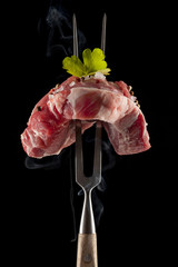 raw steak on a big meat fork on black background