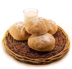 Fresh baked homemade bread in a wicker wood basket with a glass of milk