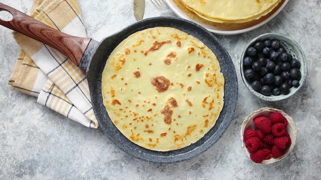 Delicious pancakes on stone frying pan. Placed on table with various ingredients on side. With fresh fruits, black coffee cup. Flat lay. View from above.
