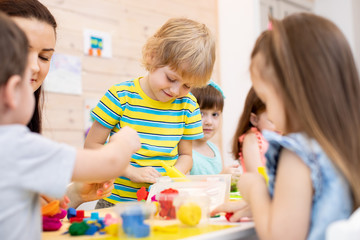 Children dough play in daycare centre. Kids with teacher mold from plasticine in kindergarten. Little students knead modeling clay with hands in preschool.