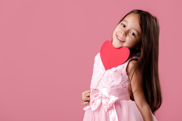 smiling cute little girl in a pink dress holding a paper heart on a pink background. St. Valentine's Day