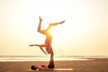 Fototapeta na wymiar Two people practicing yoga in the sunset light on goa india beach. female and male acro yogi tantra flying copyspce