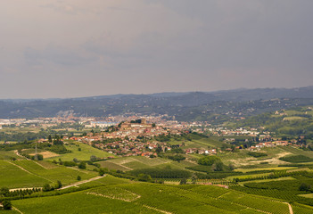 Fototapeta na wymiar Panoramic view of hills and valleys with a medieval village and cloudy sky in springtime, Roddi d'Alba, Langhe, Piedmont, Italy