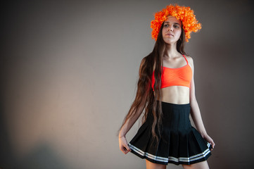 young girl with long hair in orange wig and top in carnival costume poses for the camera. Cosplay, anime, fantasy