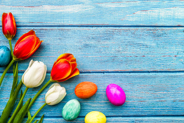 white and red tulips bouquet with colored eggs on blue wooden planks background, copy space, top view