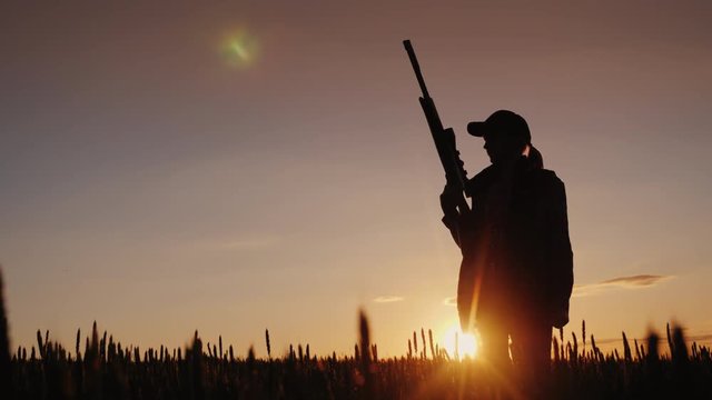 Silhouette of a woman with a gun in her hands. Hunter in the field at sunset