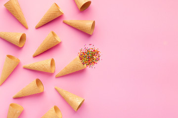 Empty ice-cream waffle cones and colorful sprinkles on pink background,