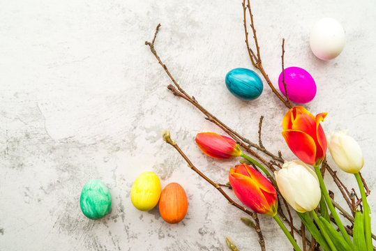 pussy willow branches and tulips with colored eggs on white marble background background, copy space, top view