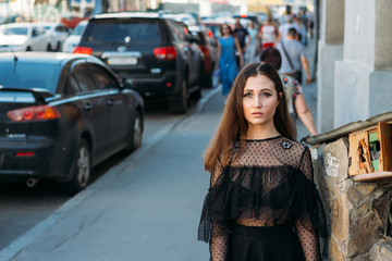 Fototapeta na wymiar portrait of a girl, brunette, in a black dress, in the arch, in the city. posing, walking. alone in the crowd, loneliness