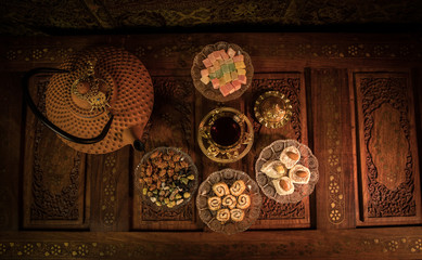 Arabian tea in glass with eastern snacks on vintage wooden surface. Eastern tea concept. Low light lounge interior with carpet. Empty space.